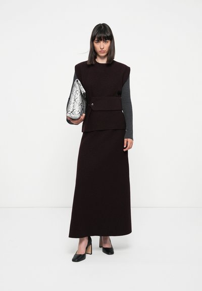 Burgunderfarbiges Strickkleid mit strukturiertem Schulterdesign, kombiniert mit einer silbernen Schlangenleder-Clutch und schwarzen Blockabsatzschuhen.