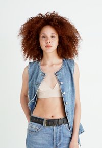 Denim brez rokavov z gumbi na sprednji strani, svetlo modra pranja in neobdelan rob. V kombinaciji z bež majico in kratkimi hlačami z visokim pasom, zavarovano s črnim pasom.