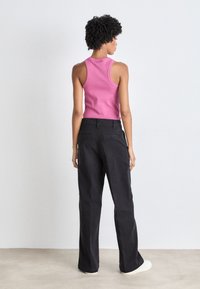 Top senza maniche rosa e pantaloni a gamba larga neri. Il top ha una vestibilità aderente; i pantaloni presentano passanti per cintura e una silhouette rilassata. Calzature leggere.