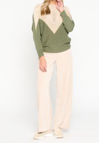 Suéter de punto verde con un cuello beige de estampado, combinado con pantalones de pana anchos de un beige claro y zapatillas crema.
