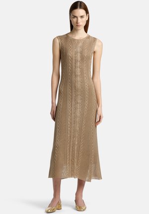 Beige gebreid jurkje met een mouwloos ontwerp, gekenmerkt door ingewikkelde texturen en patronen. Halflang met een recht model, gecombineerd met gouden schoenen.