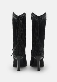 Botas de tacón alto de ante negro con detalles de flecos, tachuelas en forma de pirámide y acentos texturizados en el puño y los laterales.