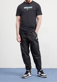 Svart kortärmad t-shirt med färggård "JUST DO IT"-logotyp, ihop med svarta slick joggers och svarta och vita sneakers.