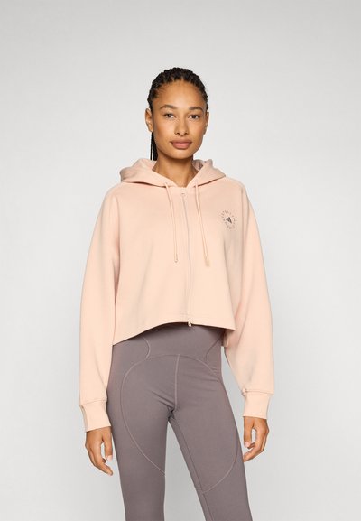 Veste à capuche raccourcie zippée en coton rose doux avec un logo sur le devant, accompagnée de leggings gris taille haute avec des accentuations de coutures courbes.