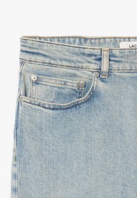 Jeans in denim azzurro chiaro con taglio dritto, dotati di vita standard, tasche frontali e hardware tono rame. Texture morbida.