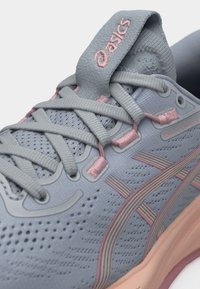 Ανοιχτό γκρι και ροζ παπούτσι για τρέξιμο ASICS με επάνω μέρος από δίχτυ, γκρι κορδόνια και σόλα ροδακινί χρώματος, που δείχνει λεπτομέρειες από το πλάι και από πάνω.
