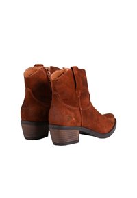Botas de tobillo de ante marrón con punta redondeada, cremallera lateral y un tacón bajo apilado. Las costuras son visibles a lo largo de las uniones.
