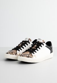 Sneaker bianche con un tallone nero testurizzato, parte anteriore con stampa a serpente, lacci neri e suola in gomma crema. Presenta il logo sulla linguetta.