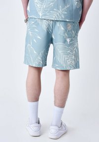 Pantalones cortos de color azul claro con un patrón de hojas blancas, que cuentan con un bolsillo trasero. Combinados con calcetines blancos y zapatillas, mostrando una tela texturizada.