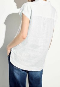Camicia di lino azzurro chiaro con yoke sul retro e maniche corte, caratterizzata da una vestibilità comoda e fessure laterali, abbinata a pantaloni in denim blu scuro.