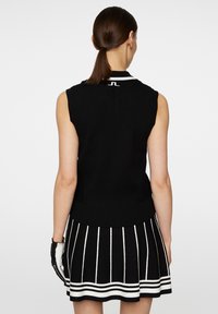 Black sleeveless sweater with a ribbed texture, featuring a white collar and subtle logo at the back. Paired with a striped black-and-white skirt.