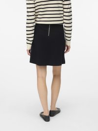 Juoda sijonas tiesaus silueto, su matoma užtrauktuko detalė nugarinėje pusėje. Derinamas su dryžuotu megztiniu ir juodais bateliais.