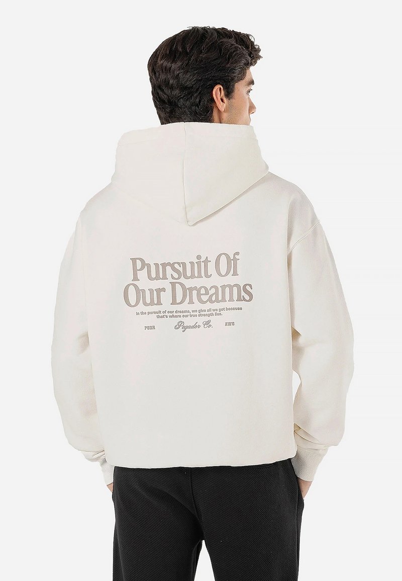 Sudadera crema clara con una gran impresión en la parte posterior en texto beige oscuro. Cuenta con capucha con cordón y puños acanalados. Corte casual y oversize.