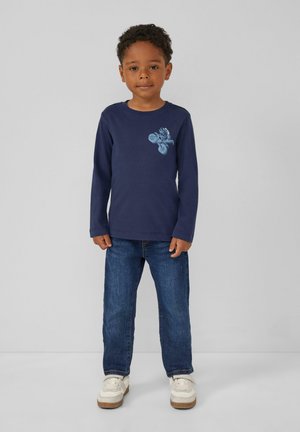 Marineblaue Langarm-T-Shirt mit hellblauem Grafikdesign; kombiniert mit blauen Jeans und weißen Sneakers; lässiger Schnitt und weiches Baumwollmaterial.