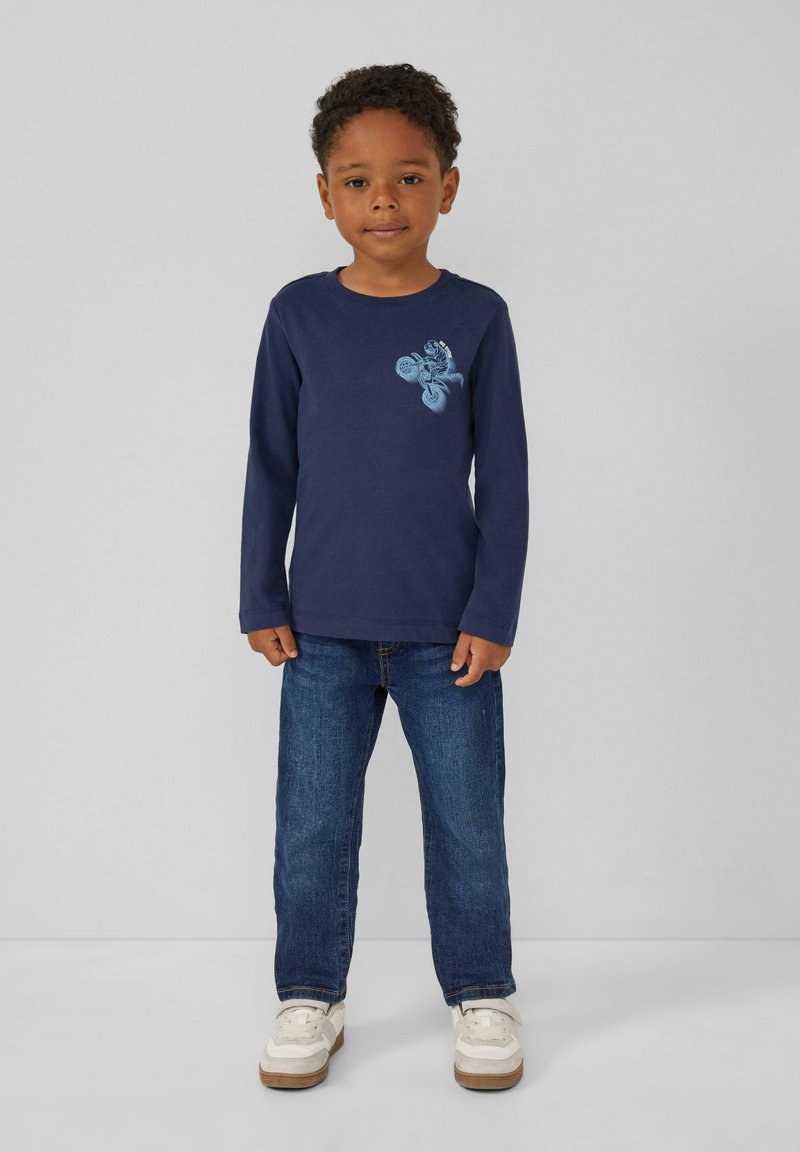 Granatowa koszulka z długim rękawem z jasnoniebieskim wzorem; w połączeniu z niebieskimi dżinsami i białymi trampkami; luźny krój i miękki materiał bawełniany.