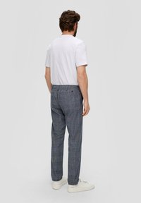 Grijze geruite broek met een traditionele pasvorm, voorzien van subtiele blauwe en oranje lijnen, gecombineerd met een eenvoudige witte T-shirt en witte sneakers.
