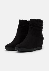 Bottines en daim noir avec un design plissé, semelle compensée, fermeture éclair latérale et semelle en caoutchouc noir texturé. Finition lisse avec des accents minimaux.