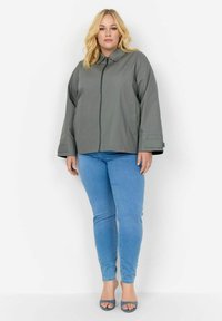 Siva zip-up jakna s ovratnikom, prostran kroj in dolgi rokavi. V kombinaciji z svetlo modrimi ozkimi kavbojkami in sivimi sandali z odprtim prstom.