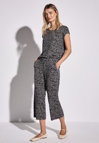 Černobíle vzorovaný outfit obsahující tričko s krátkým rukávem a zkrácené kalhoty s kapsami, vyrobený z měkké, lehké tkaniny.