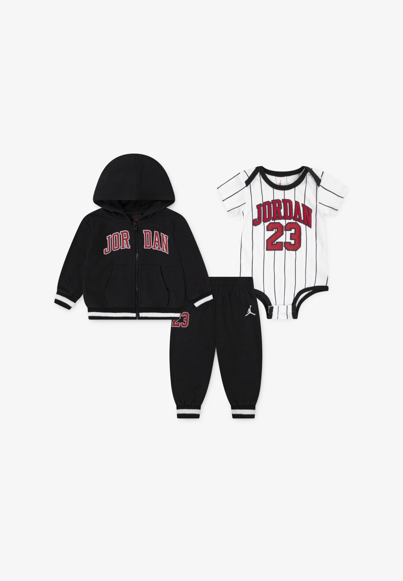 Melna džemperis ar rāvējslēdzēju un ar "JORDAN" logotipu, atbilstošas melnas bikses ar logotipu, kā arī balts kombinezons ar svītrām, kas izceļ "JORDAN 23" dizainu.
