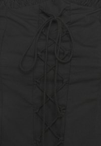 Vêtement en tissu noir avec un devant à lacets texturé, comportant des cordons noirs et une taille froncée. Texture lisse sans motifs apparents.