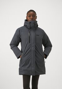 Tmavě šedá izolovaná parka s vysokým límcem, kapsami na zip a detailem loga. Disponuje elegantním designem a odolnou tkaninou.