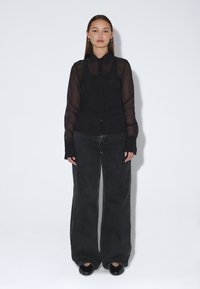 Musta läpikuultava nappitakki, jossa pitkät hihat, yhdistetty leveälahkeisiin harmaisiin farkkuihin. Mallilla on mustat korotetut kengät ja hopeiset rengaskorvakorut.