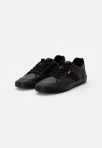 Une paire de baskets basses noires avec lacets et une étiquette rouge Levi's sur le côté, présentée sur un fond blanc.