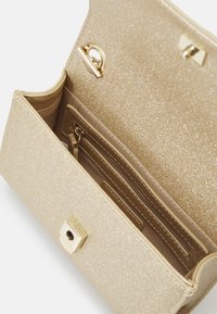 Borsa glitter dorata con una texture liscia, dotata di una tasca interna con zip e slot per carte. Chiusura assicurata da una fibbia metallica quadrata.