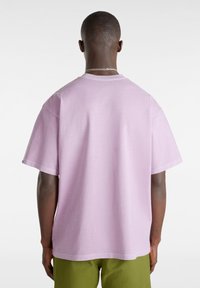 T-shirt viola chiaro a maniche corte con vestibilità comoda, scollo rotondo e dettagli di cucitura minimali. Indossato con pantaloni verdi.