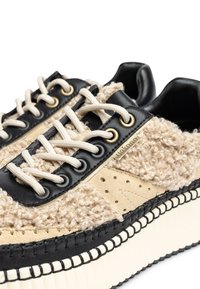 Sneaker mit einem flauschigen beigefarbenen Obermaterial, schwarzen Lederakzenten und cremefarbenen Schnürsenkeln. Mit goldenen Ösen und einer strukturierten weißen Sohle mit Nahtdetail.
