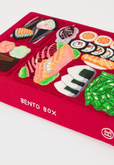 Czerwona książka z tkaniny zatytułowana "Bento Box" z haftowanymi sekcjami przedstawiającymi sushi, ryby, kulki ryżowe i zielone liściaste warzywa.