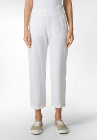 Pantalones de lino blancos con un corte relajado, que presentan bolsillos delanteros y puños enrollados. Textura suave y tela ligera, combinados con zapatos de lona.