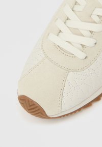 Αθλητικό παπούτσι ανοιχτού μπεζ χρώματος με επάνω μέρος από καστόρι και υφασμάτινο με σχέδιο αστεριού, λευκά κορδόνια και καφέ λαστιχένια σόλα.