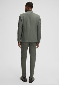 Completo verde oliva realizzato in tessuto strutturato. Presenta una vestibilità sartoriale, blazer monopetto, tasche inclinate e pantaloni a taglio slim con piega.