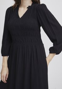 Schwarzes Kleid mit einem gerafften Oberteil, langen Puffärmeln und einem V-Ausschnitt. Verfügt über einen strukturierten Stoff und Raffungselemente an der Taille.