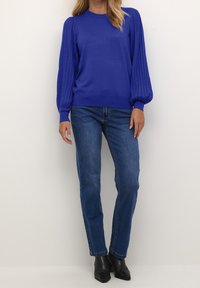 Jasnoniebieski sweter z prążkowanymi bufkami na rękawach, zestawiony z prostymi niebieskimi dżinsami i czarnymi botkami za kostkę. Gładka tekstura i prosty design.