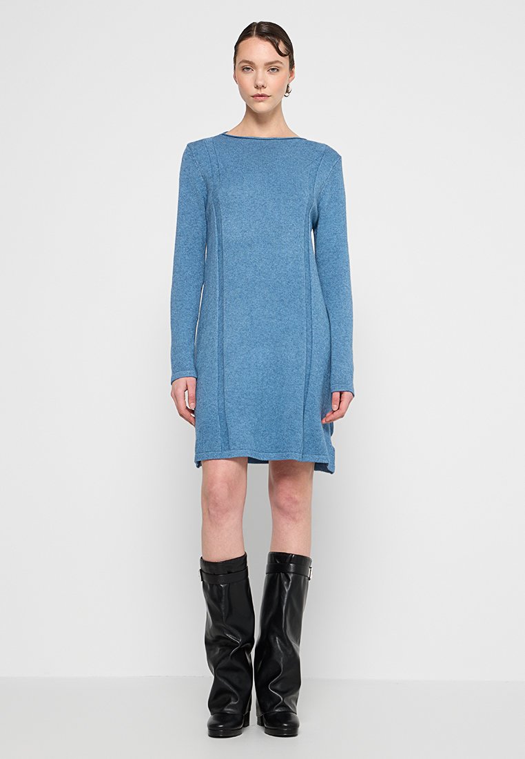 Robe tricotée bleu à manches longues avec un décolleté carré et des coutures latérales. Portée avec des bottes en cuir noir jusqu'aux genoux, créant un look contrasté.
