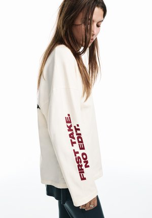 Bluză cu mâneci lungi, crem, cu text bordo „FIRST TAKE. NO EDIT.”; are un croi lejer și o textură moale.