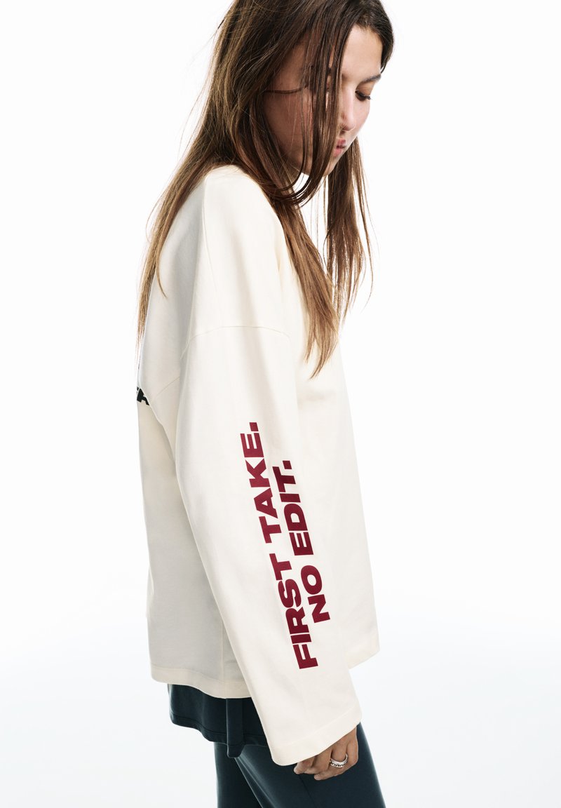 Crèmekleurige sweatshirt met lange mouwen en bordeauxrode tekst "FIRST TAKE. NO EDIT."; heeft een ontspannen pasvorm en een zachte textuur.
