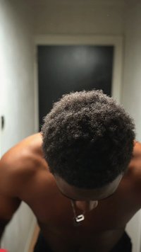 Close-up van krullend donker haar, geaderd en dicht, boven blote schouders en nek met een zilveren hanger. Neutrale achtergrond met gedimd licht.