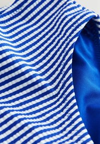 Kék és fehér csíkos szövet, hullámos vonalakkal, sima textúrával. A belső réteg egyenletes kék anyaggal rendelkezik, gondosan varrva.