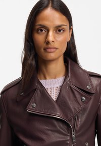 Burgundy leather motorcycle jacket with silver hardware, zip closure, and notched collar, worn over a light knitted sweater.