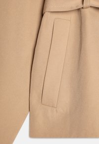 Beige trenchcoat stoff med diagonalt vevemønster. Har en sidelomme og brettet krage. Glatt tekstur med skreddersydd design.