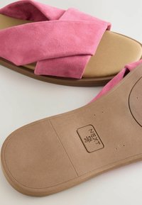 Roze antilopne sandale s križnim trakama, s tamnim jastučićem za stopala i teksturiranom gumiranom potplatom, s otisnutim logotipom brenda na dnu.