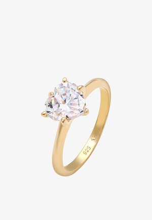 Bague plaquée or avec une grande pierre transparente en forme de cœur, maintenue par quatre griffes ; l'anneau est lisse avec une finition polie.