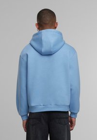 Svetlo modra kapuca s prostorno kapuco, rebrastimi manžetami in robom. Gladek mešanica bombaža; oblečena z temno sivo jeansom.