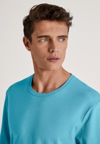 Lichtblauw, rondhals t-shirt gemaakt van soepel stof. Heeft lange mouwen en een eenvoudig ontwerp, met de nadruk op comfort en pasvorm.
