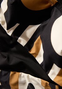 Slipdress gemaakt van een gladde stof met een gedurfde patroon van zwarte, witte en gouden vormen met een matte textuur. Zichtbare accentnaden.