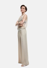 Beige strikket tanktop med en løs pasform, parret med højtaljede, brede beige bukser og remsandaler; blød tekstur hele vejen igennem.